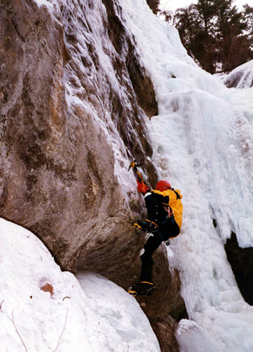 Climber mantling the base of <i>Low Deductible</i> verigris ice